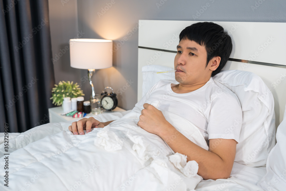 sick man is headache and using thermometer to checking his temperature in bed sick man is headache and using thermometer to checking his temperature in bed