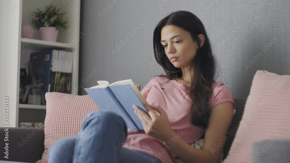 Beautiful young woman reading a sad book while sitting on sofa Beautiful young woman reading a sad book while sitting on sofa