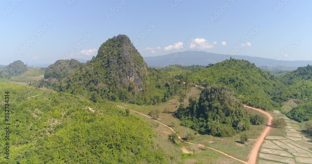 Aerial shot of green landscape against blue sky on sunny day, drone panning over dirt road amidst plants and trees in forest - Luang Prabang, Laos Aerial shot of green landscape against blue sky on sunny day, drone panning over dirt road amidst plants and trees in forest - Luang Prabang, Laos