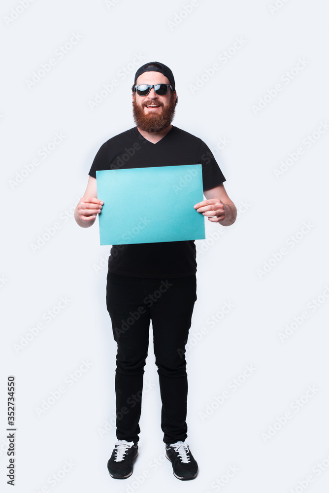 Full length photo happy bearded man holding blue blank paper over white Full length photo happy bearded man holding blue blank paper over white
