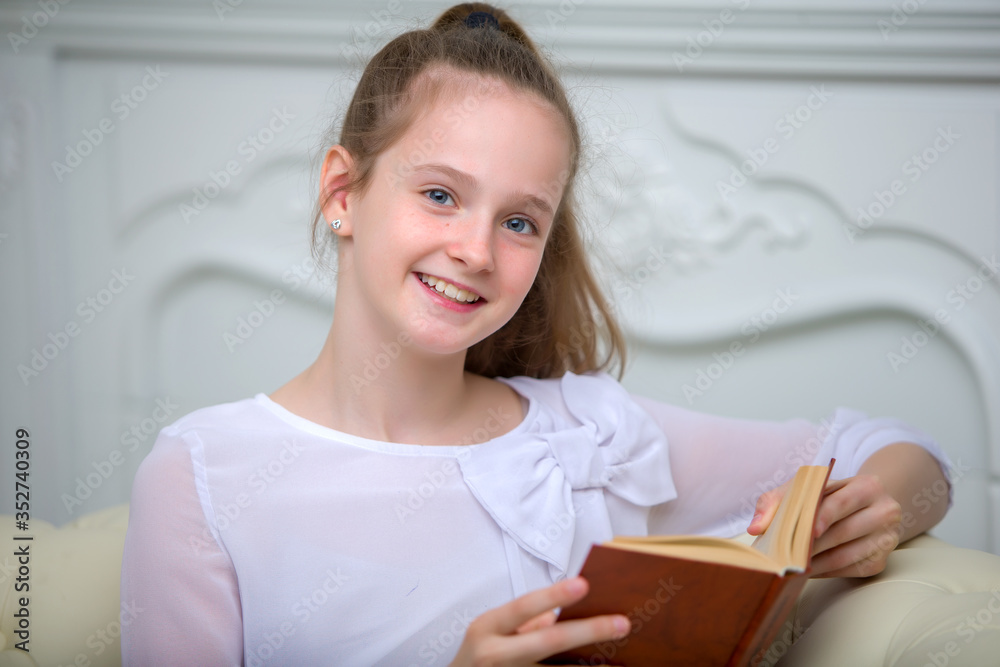An adorable little girl sits on a sofa and reads a book enthusiastically. An adorable little girl sits on a sofa and reads a book enthusiastically.