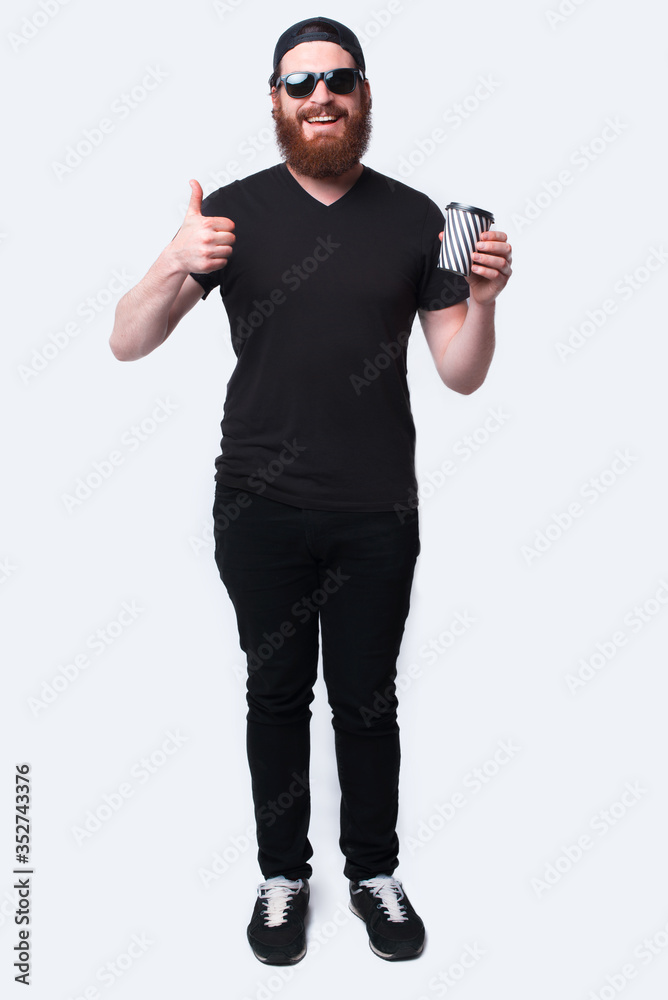 Full length photo smiling bearded man holding cup of coffee to go Full length photo smiling bearded man holding cup of coffee to go