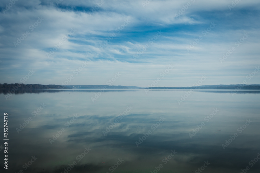 Reflections of Clouds in the Sky on calm, tranquil Water with Trees on Horizon and plenty of Copy Space