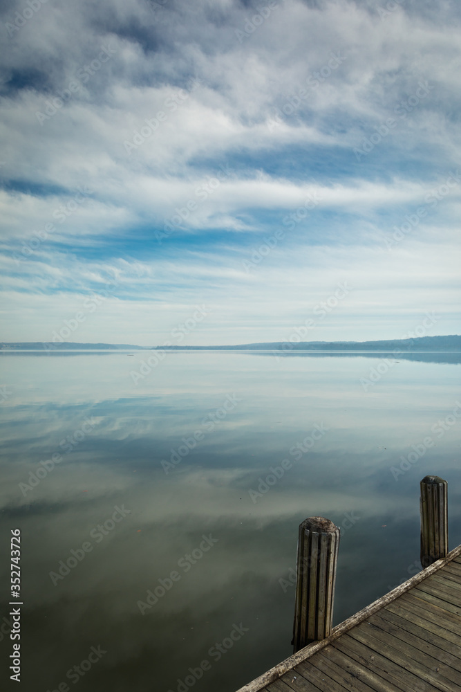 Naklejka premium Reflections of Clouds in the Sky on calm, tranquil Water with wooden Pier in Foreground and lots of Copy Space