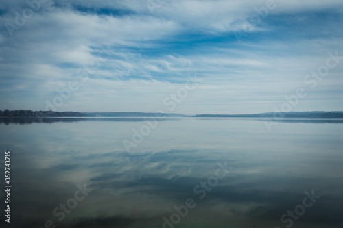 Reflections of Clouds in the Sky on calm  tranquil Water with Trees on Horizon and plenty of Copy Space