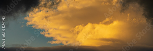 Panorama dramatic clouds illuminated rising of sun floating blue sky. Natural weather, meteorology background. Soft focus, motion blur sky majestic cloudscape.