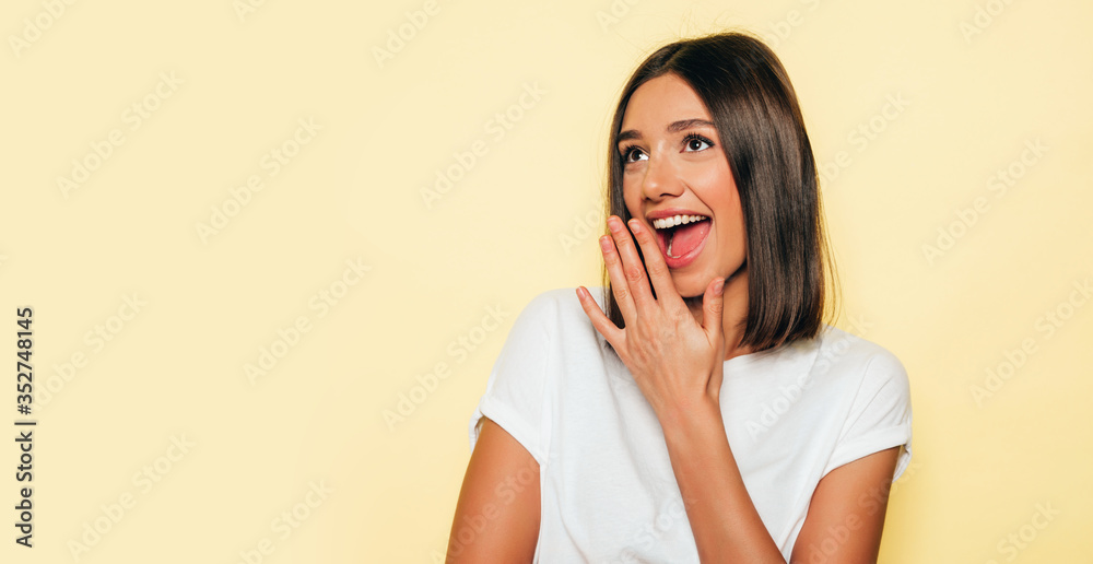 Young beautiful woman looking at camera.Trendy girl in casual summer white T-shirt and jeans shorts.Positive female shows facial emotions.Shocked and surprised with hands near face Young beautiful woman looking at camera.Trendy girl in casual summer white T-shirt and jeans shorts.Positive female shows facial emotions.Shocked and surprised with hands near face