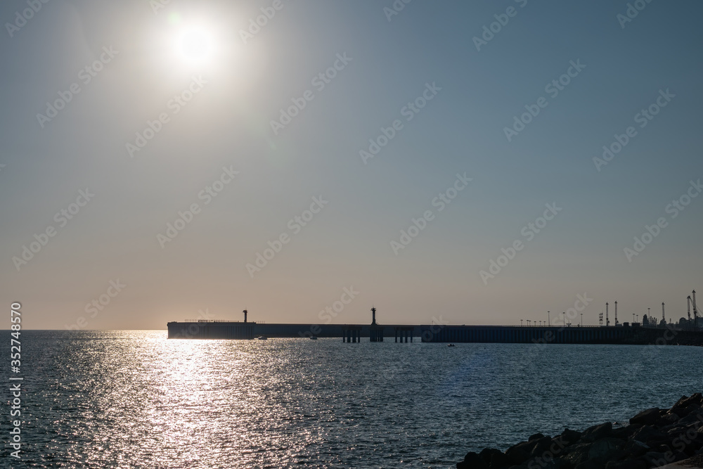 Clear sky and bright sunset at sea port with a breakwater and a lighthouse