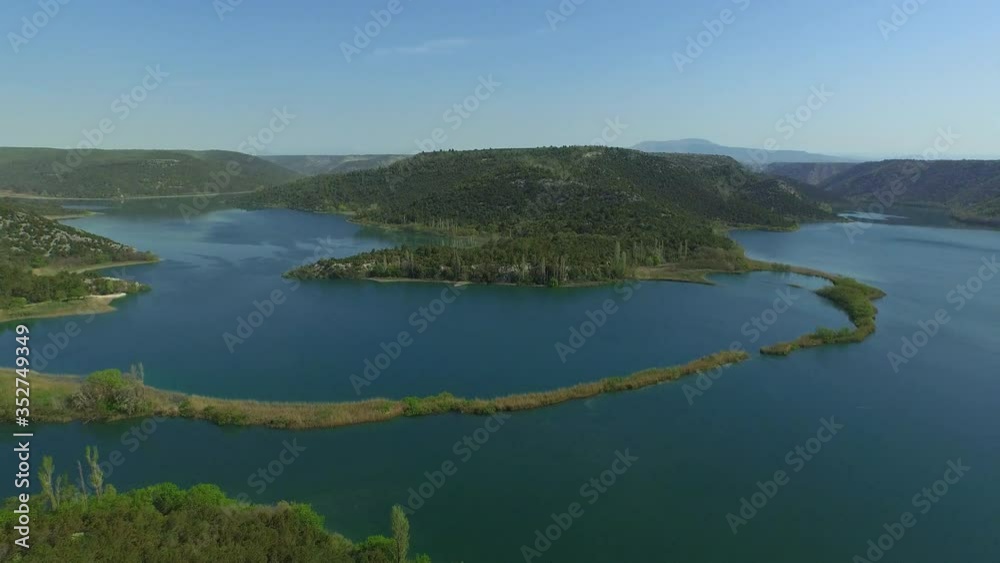 Aerial panning shot of mountains covered with trees by river against blue sky - Krka, Croatia Aerial panning shot of mountains covered with trees by river against blue sky - Krka, Croatia