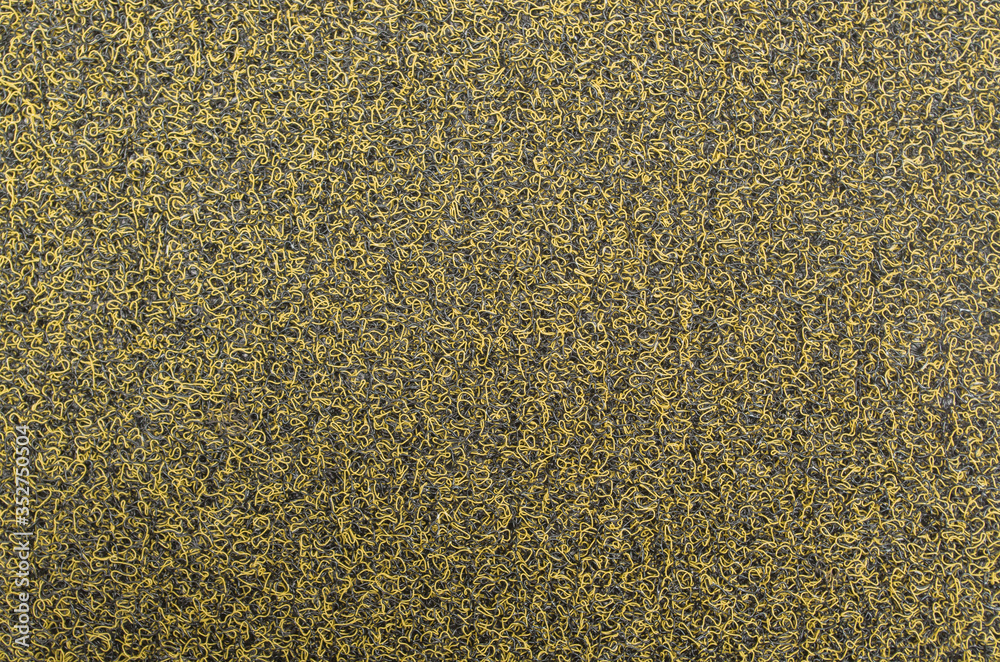 Fragment of floor covering of dirt-proof entrance mat, the surface of which consists of yellow and black rigid synthetic fibers in form of spaghetti. Abstract, two-tone futuristic design background. Fragment of floor covering of dirt-proof entrance mat, the surface of which consists of yellow and black rigid synthetic fibers in form of spaghetti. Abstract, two-tone futuristic design background.