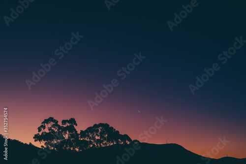 sunset sky with blue to purple to orange gradient colors  unedited  and moon over the hills with eucalyptus tree silhouettes