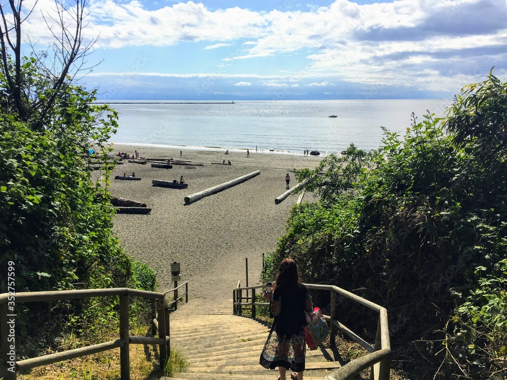 Φωτογραφία a young woman walking down the stairs facing outwards towards wreck beach in Vancouver, BC