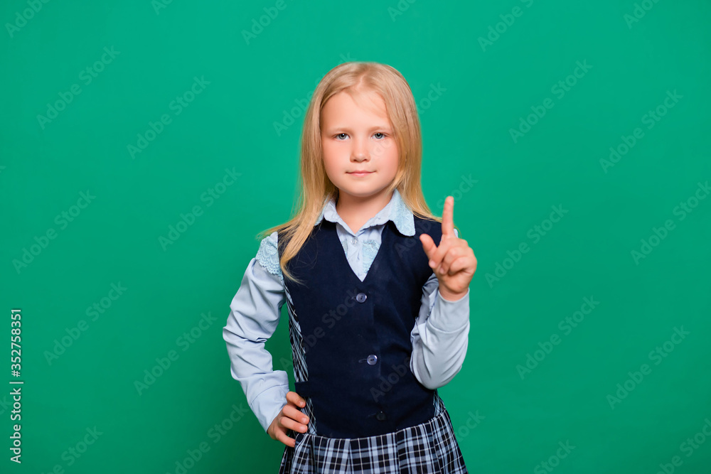 Little girl in school uniform holds forefinger up isolated on a green background. A gesture of attention, an idea.
Little girl in school uniform holds forefinger up isolated on a green background. A gesture of attention, an idea.