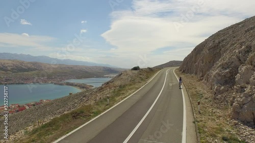 Aerial: Man cycling on road by rock formation near sea against sky, person riding on highway during sunny day - Pag, Croatia photo