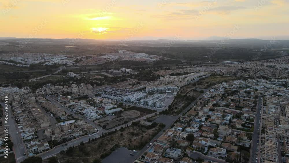 Aerial view with a drone of the resort of Orihuela-Costa on the Mediterranean coast at sunset. In the foreground there are many residential complexes and in the background a sunset over the mountains.