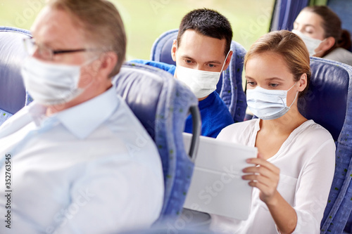 transport, tourism, road trip, technology and people concept - couple wearing face protective medical masks for protection from virus disease with tablet pc in travel bus