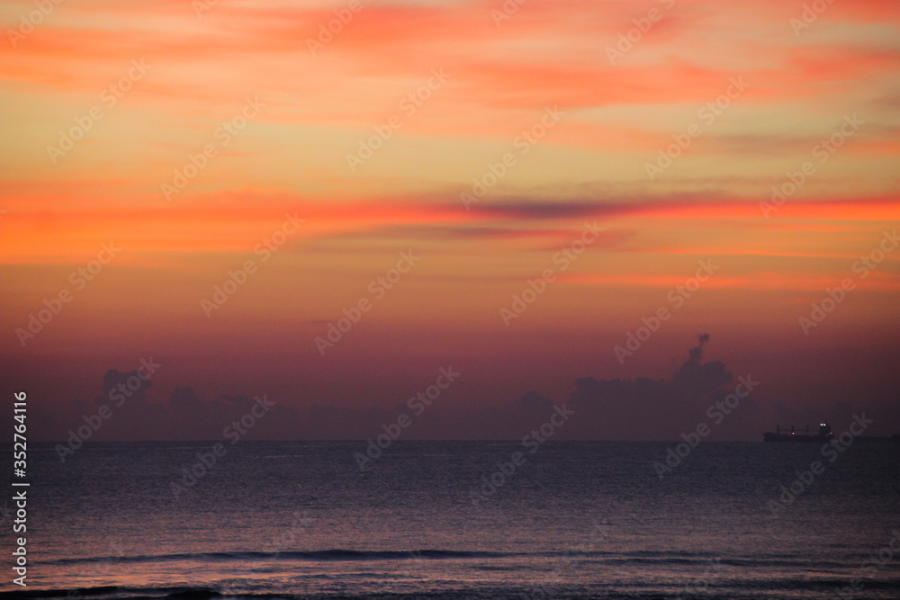 Hazy image of the orange sky above the ocean horizon with a ship on the bottom right.