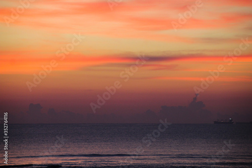 Hazy image of the orange sky above the ocean horizon with a ship on the bottom right.