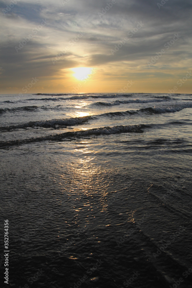 Waves lapping in sunset on the horizon. orange sun reflecting off water at the beach. water rippling portrait image.
