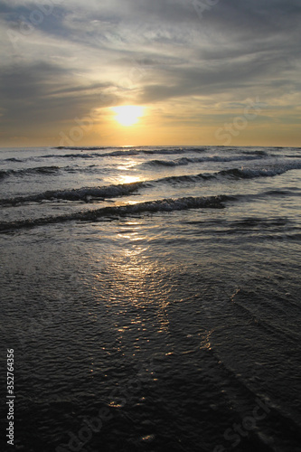 Waves lapping in sunset on the horizon. orange sun reflecting off water at the beach. water rippling portrait image.