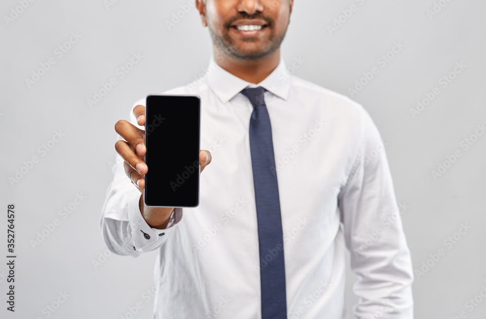 business, technology and people concept - close up of smiling indian businessman showing black smartphone screen over grey background business, technology and people concept - close up of smiling indian businessman showing black smartphone screen over grey background