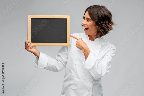 cooking, advertisement and people concept - happy smiling female chef holding black chalkboard over grey background