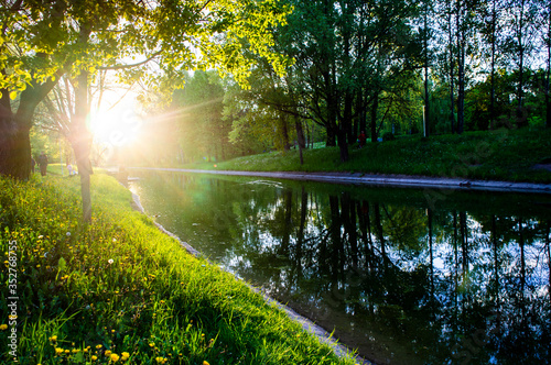 Sunny summer park with a river in the evening at sunset
