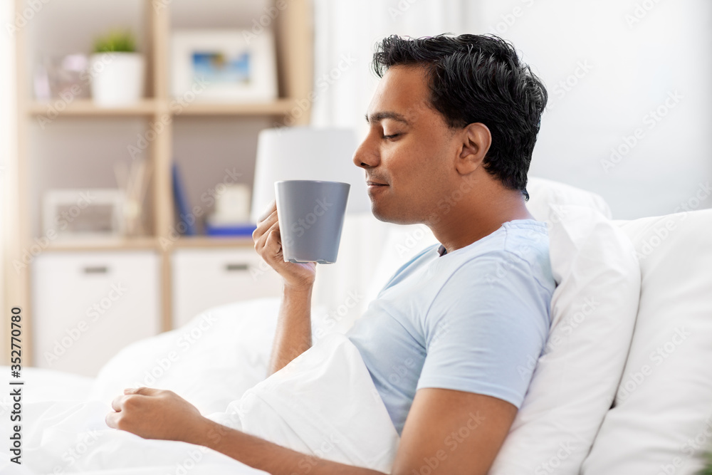 people, bedtime and rest concept - happy smiling indian man drinking coffee in bed at home people, bedtime and rest concept - happy smiling indian man drinking coffee in bed at home