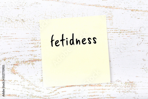 Yellow sticky note on wooden wall with handwritten word fetidness photo
