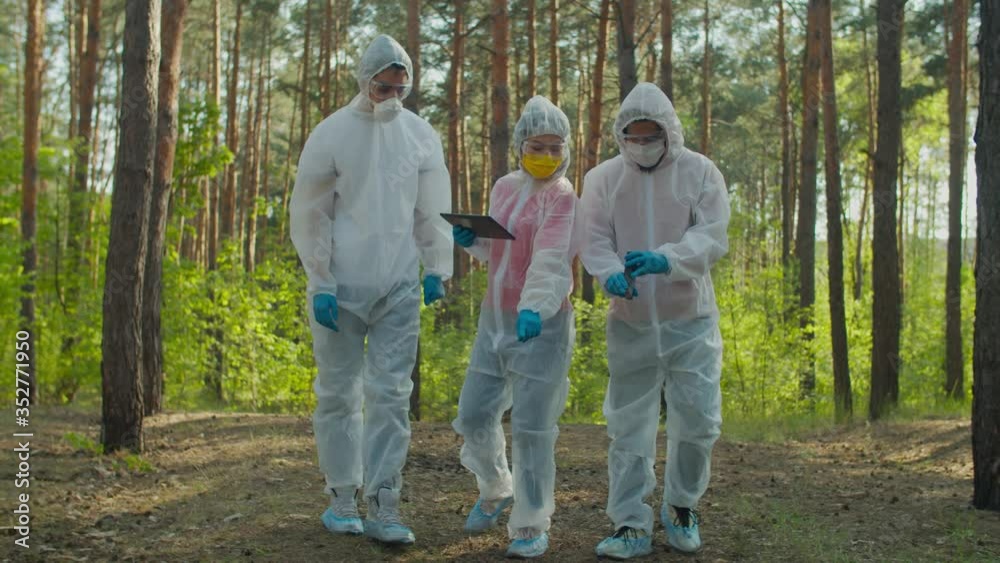 Diverse scientists in protective suits and masks with geiger counter measuring radiation level in danger zone, analyzing biohazard pollution and contamination using digital tablet. Diverse scientists in protective suits and masks with geiger counter measuring radiation level in danger zone, analyzing biohazard pollution and contamination using digital tablet.