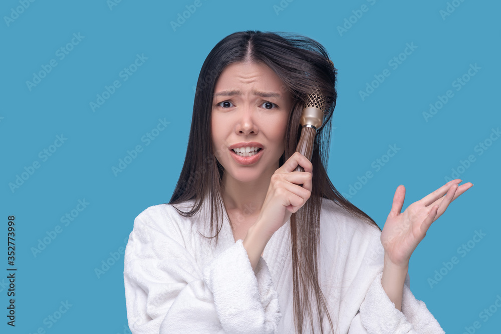 Dark-haired asian woman brushing her hair and feeling worried Dark-haired asian woman brushing her hair and feeling worried