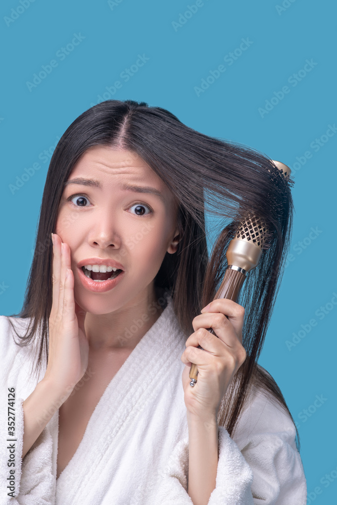 Dark-haired asian woman brushing her hair and feeling stressed Dark-haired asian woman brushing her hair and feeling stressed