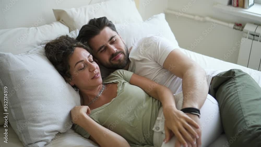 Young married couple is having good time together, lying on bed in apartment spbd. Beautiful woman and bearded hipster man talk with smiles, touch each other tenderly and lie in white room. Portrait Young married couple is having good time together, lying on bed in apartment spbd. Beautiful woman and bearded hipster man talk with smiles, touch each other tenderly and lie in white room. Portrait