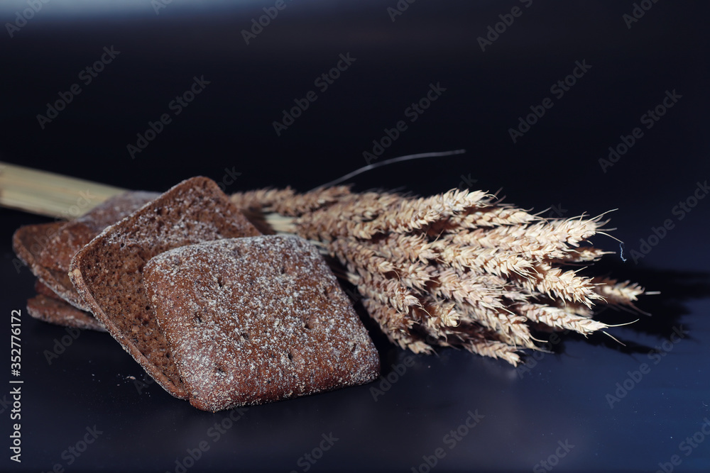 Fresh loaves of bread with wheat and gluten on a black table. Bakery and grocery concept. Fresh, healthy sorts of rye and white loaves food closeup. Fresh homemade bread with cereals.