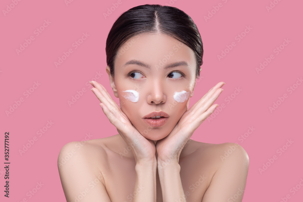 Pretty asian girl applying cream on her face Pretty asian girl applying cream on her face