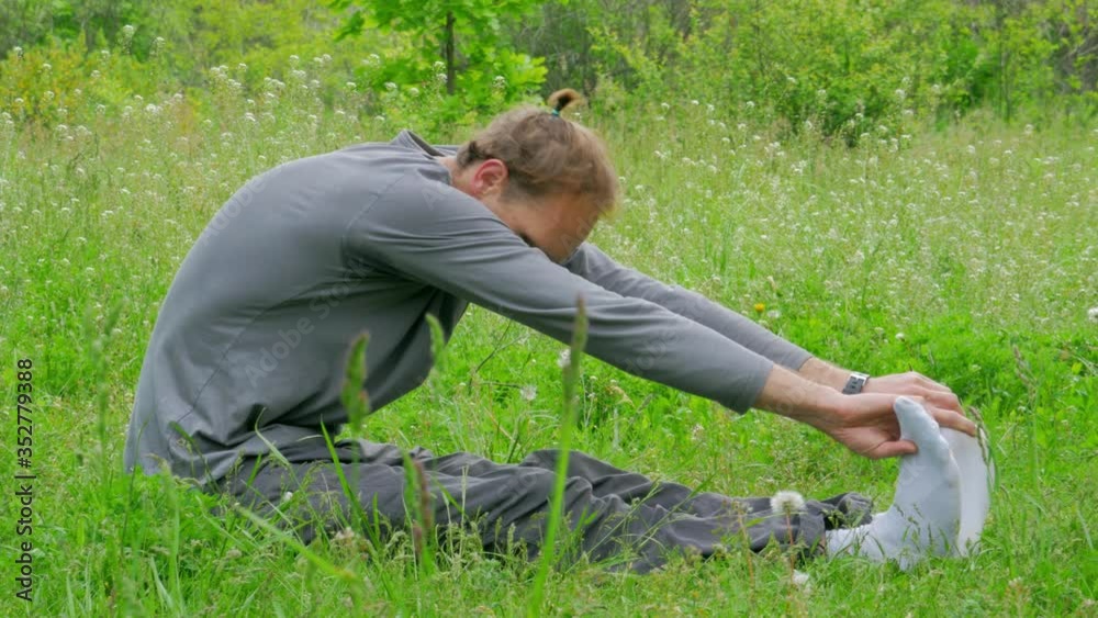 man sits on the grass and stretches his back during his yoga class man sits on the grass and stretches his back during his yoga class