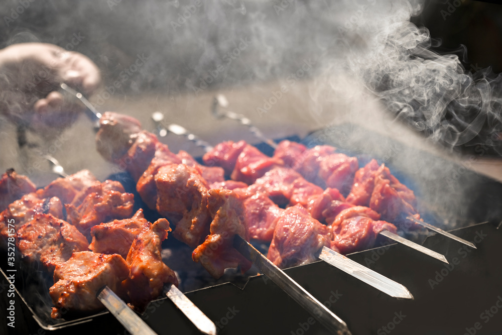 Man cooking marinated shashlik, lamb meat grilling on metal skewer. White smoke. Sale. Close up. Defocused Man cooking marinated shashlik, lamb meat grilling on metal skewer. White smoke. Sale. Close up. Defocused