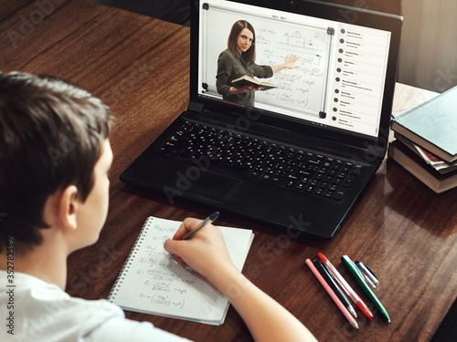 Student taking notes while watching online lesson at home during quarantine. Video conference with teacher on laptop computer. Distance and e-learning education. Modern technologies in teaching