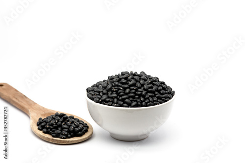 Natural black beans in a bowl and wooden spoon isolated white background. Black beans providing nutrients vitamins and iron.