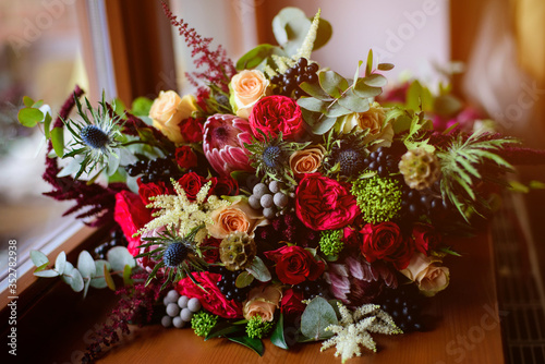 Fototapeta Naklejka Na Ścianę i Meble -  Wedding. The bride's bouquet. Wedding bouquet . A bouquet of red flowers, black berries and greens lying near the window