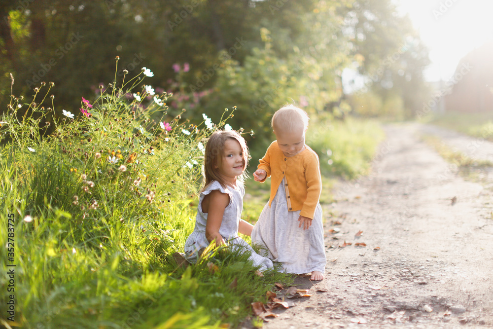 Cute Caucasian toddler kid with sister near flowers in the garden, walks with children in the park near the house and in the backyard, quarantine and stay cation