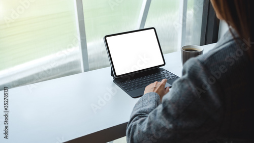 Fototapeta Naklejka Na Ścianę i Meble -  Mockup image of a woman using and typing on tablet keyboard with blank white desktop screen as computer pc , coffee cup on the table