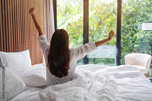 Rear view image of a woman do stretching after waking up in the morning , looking at a beautiful nature view outside bedroom window