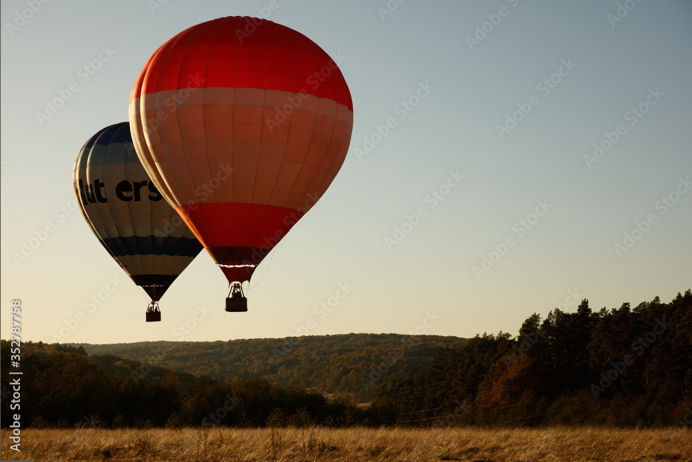 Obraz premium Group of two colorful air balloons flying over valley during summer season. Beautiful landscape and green nature. Fascinating view of air transport.