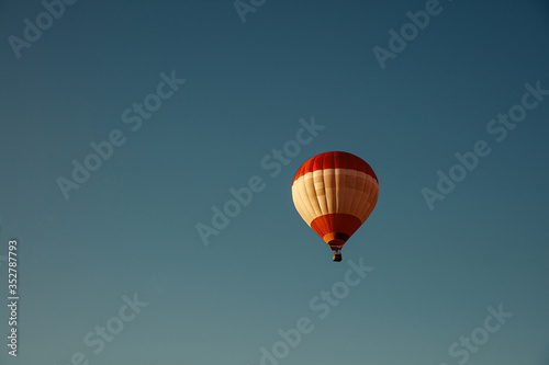 Colorful hot air balloon with basket flying high in blue sky. Natural background and wallpaper. Concept of adventure. © Tymoshchuk