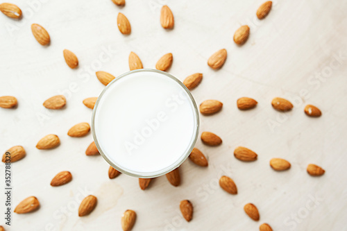 transparent mug full of milk on the background of beautifully spread almonds. Almond milk, top view