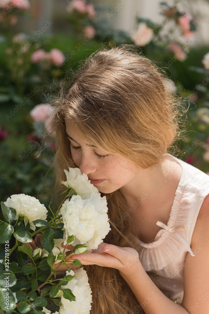 Fototapeta premium Teenager girl with waivy blonde hair smelling white garden roses