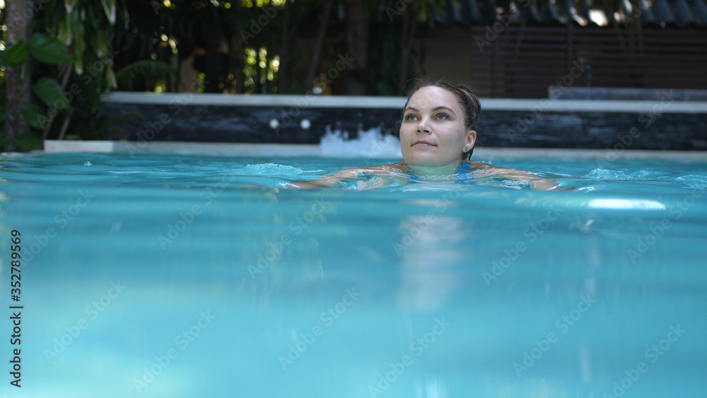 Beautiful young woman swimming in a pool at a luxury spa in tropics.