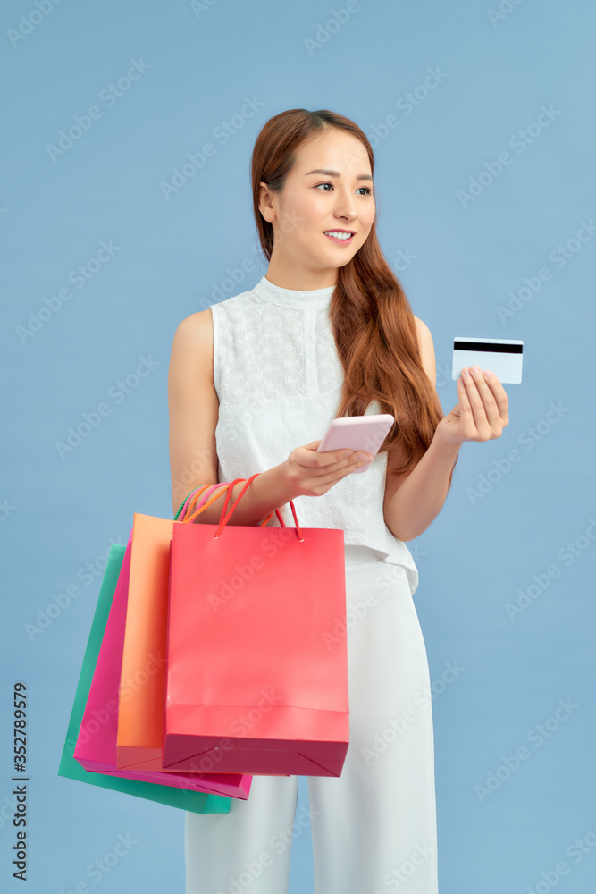 Young Asian woman with shopping bag, mobile and blank card on blue background Young Asian woman with shopping bag, mobile and blank card on blue background