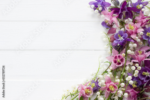 Flowers flat design. Floral composition with pink and purple Aquilegia and Convallaria flowers. Template with copy space on white wooden board
